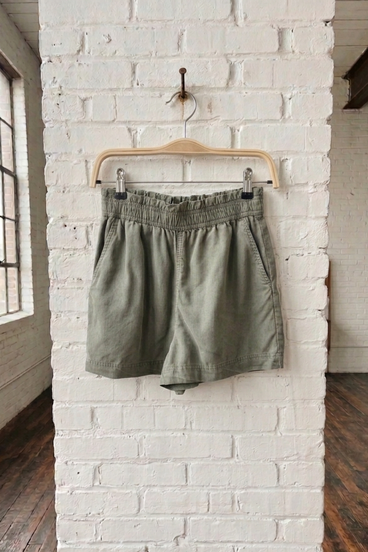 Green shorts hanging on a wooden hanger against a white brick wall.