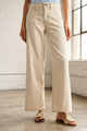 Person wearing beige wide-leg pants in a room with white brick walls and large windows.