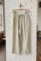 Beige pants hanging on a hanger against a white brick wall.