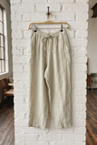 Beige pants hanging on a hanger against a white brick wall.