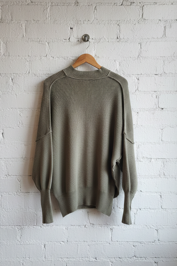 Green sweater hanging on a wooden hanger against a white brick wall.
