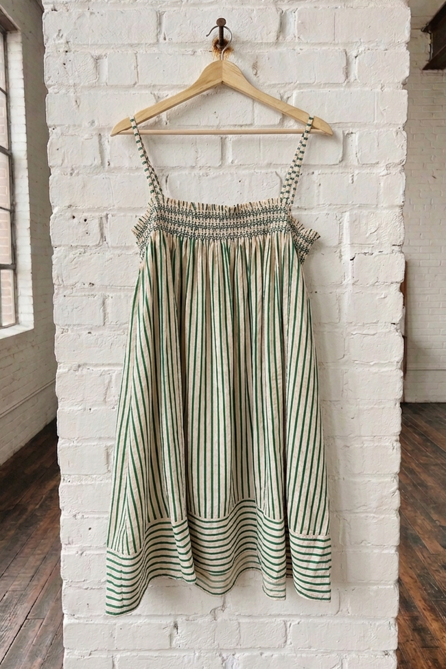 Striped dress hanging on a wooden hanger against a white brick wall.
