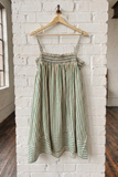 Striped dress hanging on a wooden hanger against a white brick wall.