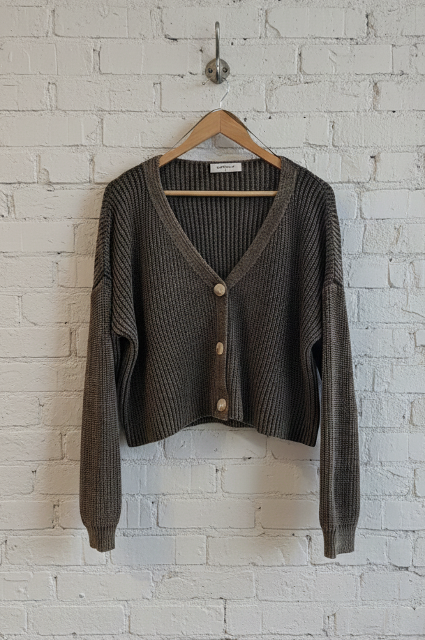 green cardigan on a hanger against a white brick wall