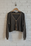 green cardigan on a hanger against a white brick wall