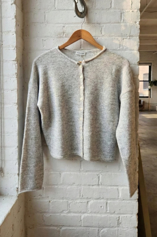 Light gray cardigan on a wooden hanger against a white brick wall.