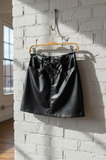 Black leather skirt hanging on a hook against a white brick wall.