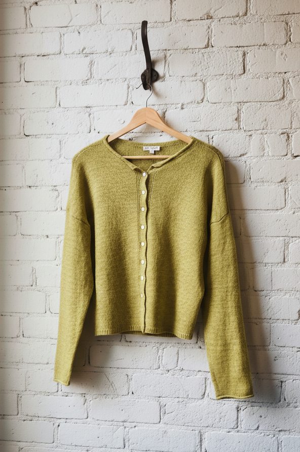 Green cardigan hanging on a hook against a white brick wall