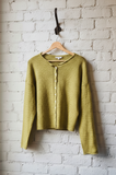 Green cardigan hanging on a hook against a white brick wall