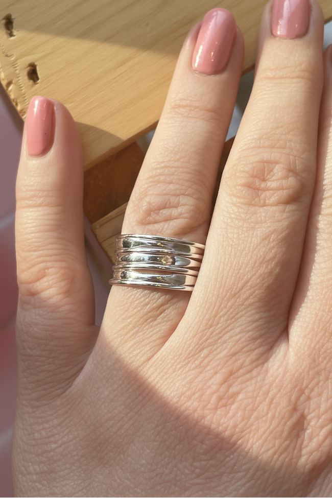 Hand wearing a silver ring with pink nail polish on a wooden surface