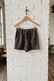 Brown shorts on a wooden hanger against a white brick wall.