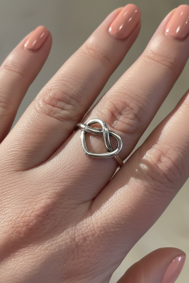 Silver heart ring on a hand with a neutral background