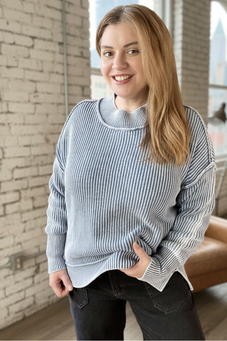 Woman wearing a striped sweater in a room with a brick wall and large window.
