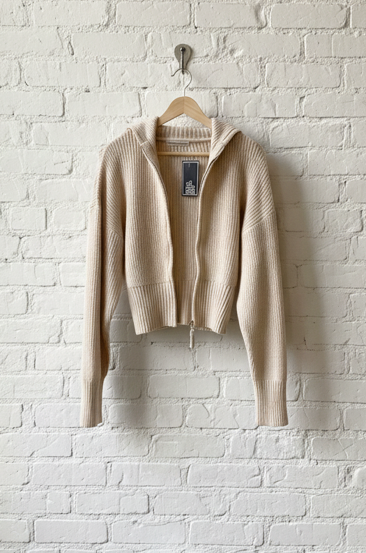 Beige sweater hanging on a hook against a white brick wall.