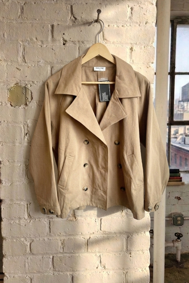 Beige trench coat hanging on a hook against a brick wall with a cityscape view.