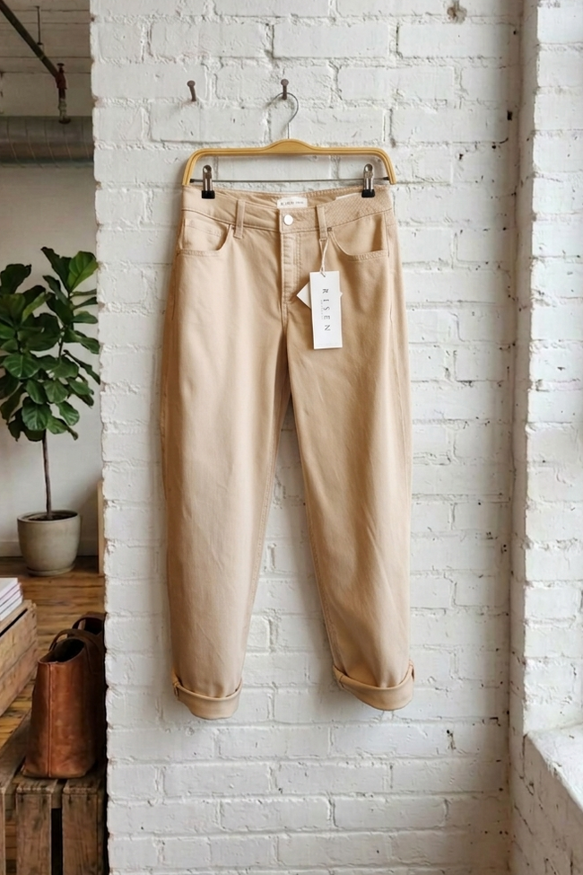 Beige pants hanging on a hanger against a white brick wall.