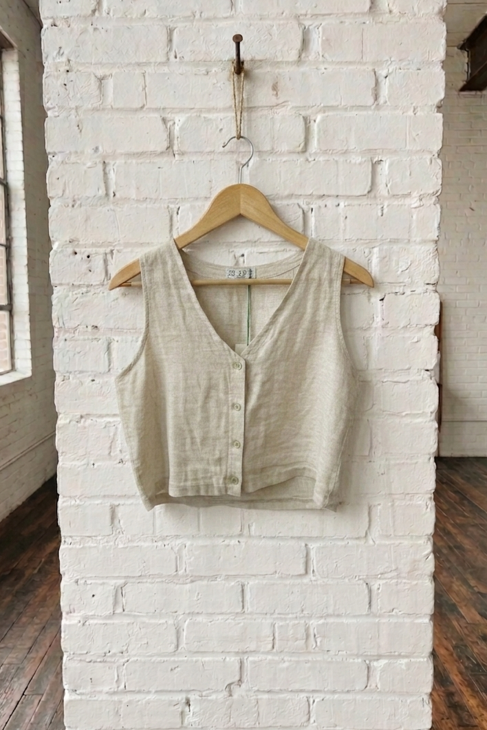 Light-colored vest on a wooden hanger against a white brick wall.