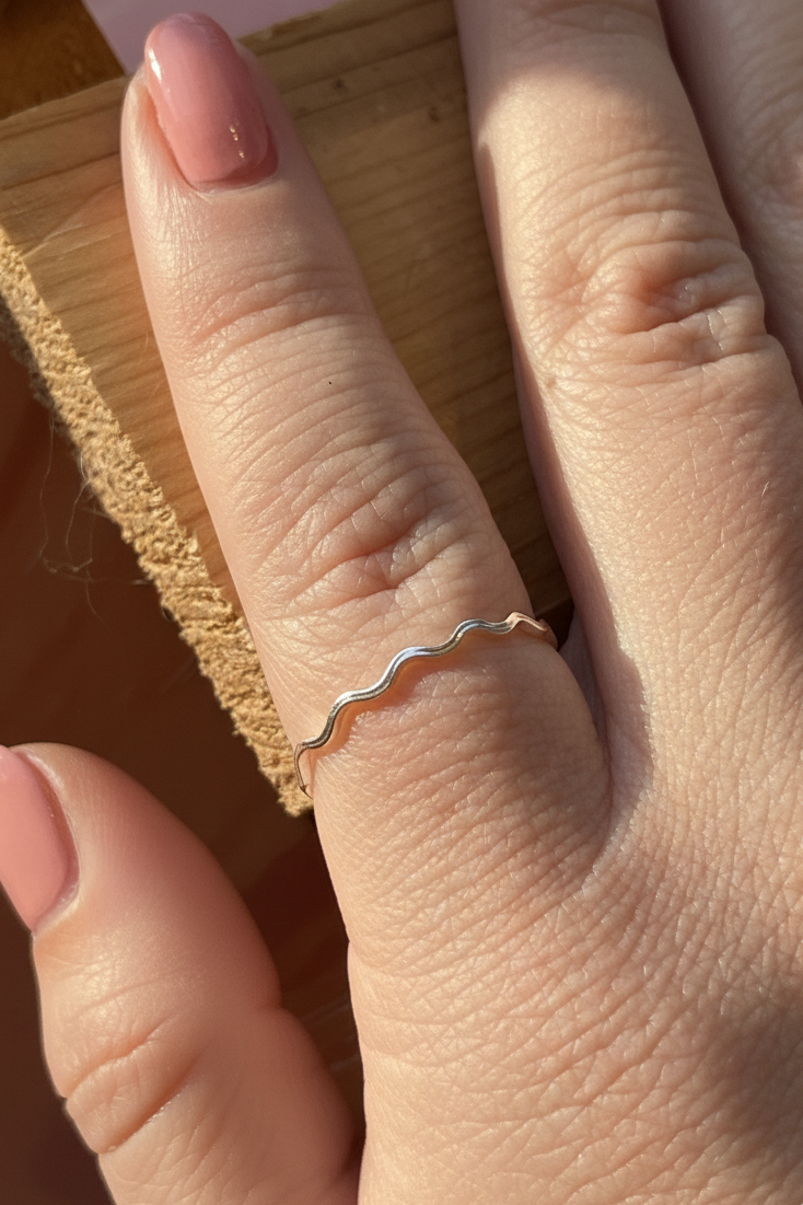 Hand wearing a gold ring with a wavy design on a wooden surface
