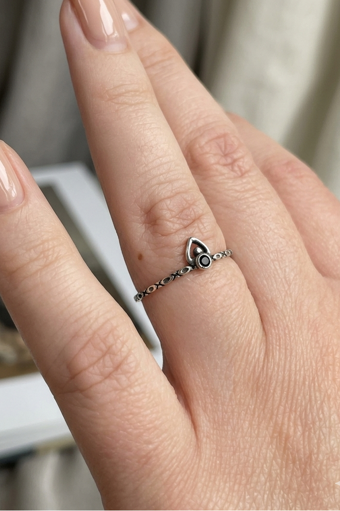 Hand wearing a delicate ring with a heart design on a neutral background