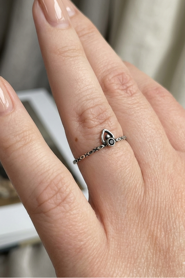 Hand wearing a delicate ring with a heart design on a neutral background