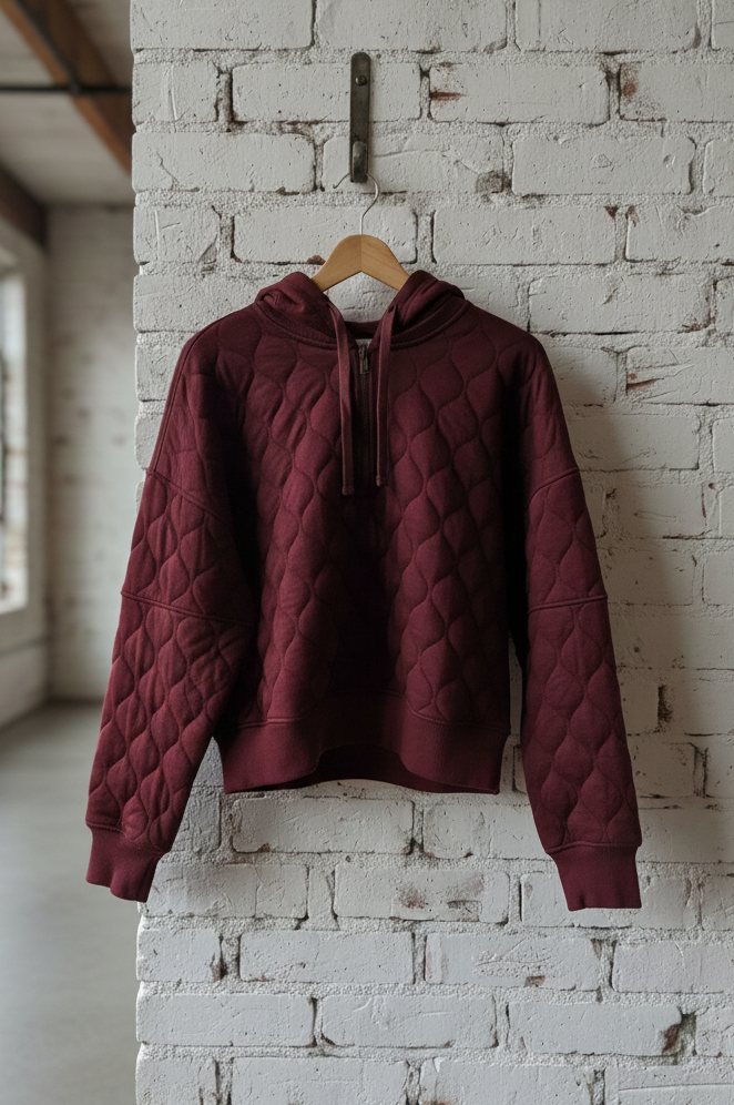 Maroon quilted jacket on a hanger against a white brick wall.