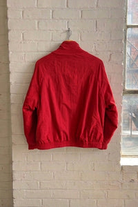 A bright red jacket hanging on a hook against a white brick wall in a loft-style room with a window and potted plants.