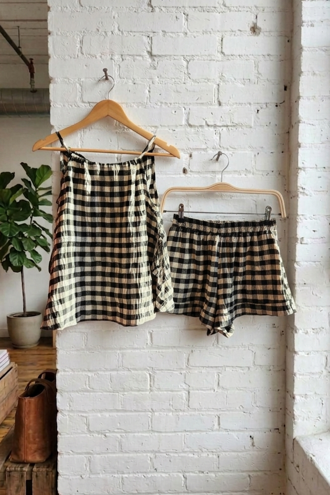 Black and white checkered top and shorts hanging on a wooden hanger against a white brick wall.