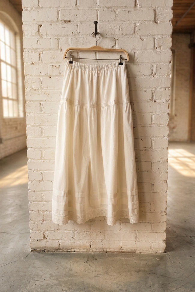 white skirt hanging on a wooden hanger against a white brick wall in a room with large windows.
