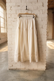 white skirt hanging on a wooden hanger against a white brick wall in a room with large windows.