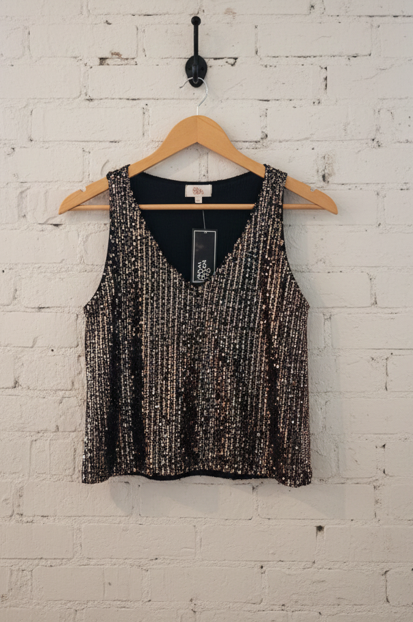 Black and gold patterned tank top on a wooden hanger against a white brick wall.