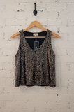 Black and gold patterned tank top on a wooden hanger against a white brick wall.