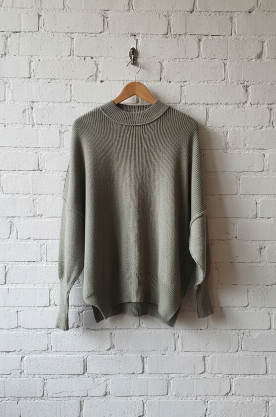 Sage Green sweater on a hanger against a white brick wall