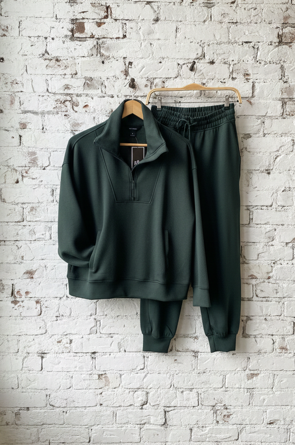 Green tracksuit hanging on a wooden hanger against a white brick wall.