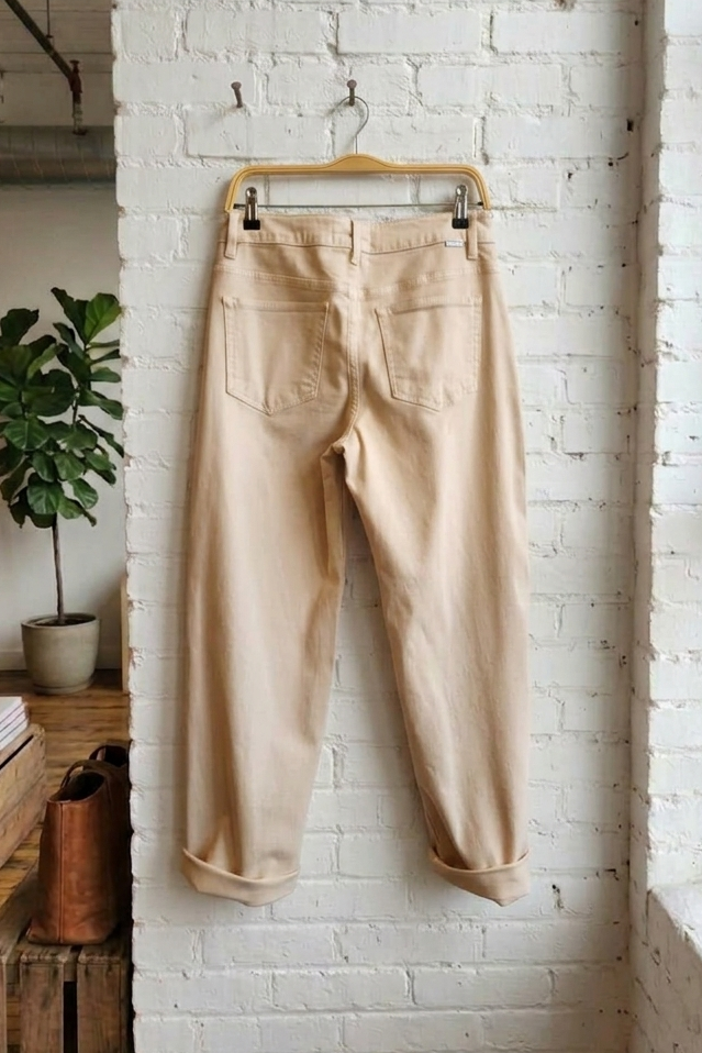 Beige pants hanging on a wooden hanger against a white brick wall.