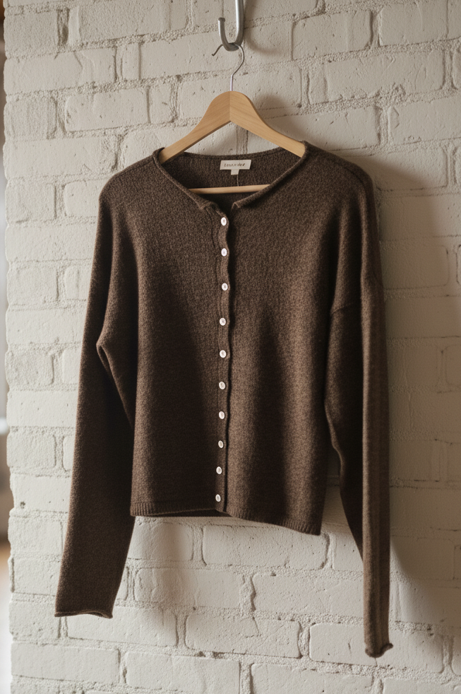 Brown cardigan on a hanger against a white brick wall