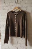 Brown cardigan on a hanger against a white brick wall