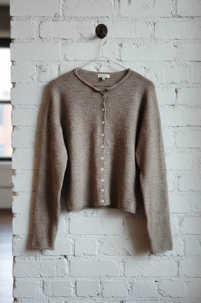 Brown sweater on a hanger against a white brick wall