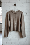 Brown sweater on a hanger against a white brick wall