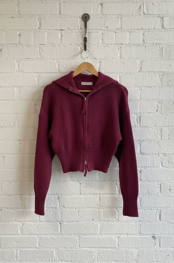 Maroon sweater on a hanger against a white brick wall.