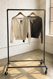 Clothing rack with two cardigans
 against a white brick wall.