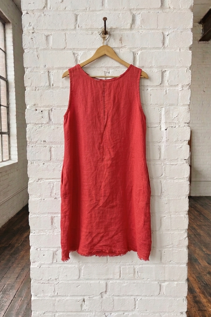 Red sleeveless dress hanging on a wooden hanger against a white brick wall.