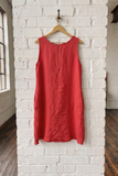 Red sleeveless dress hanging on a wooden hanger against a white brick wall.