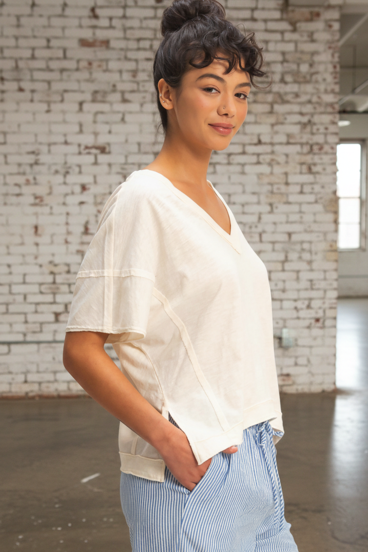 Person wearing a white top and blue pants standing against a brick wall.