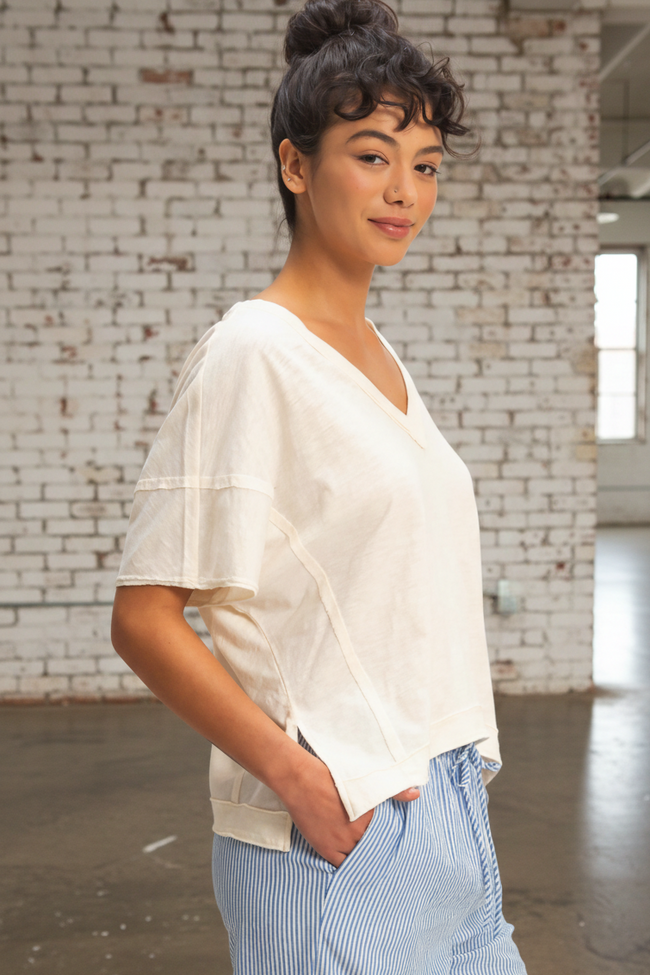 Person wearing a white top and blue pants standing against a brick wall.