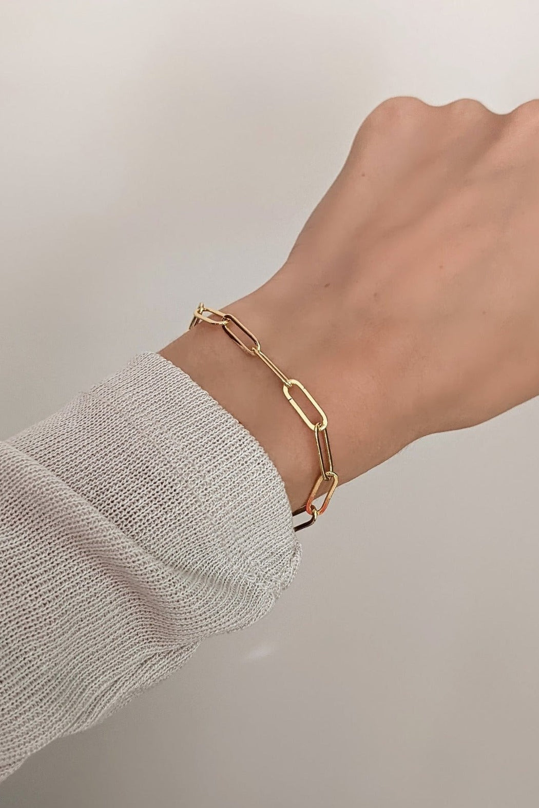 Gold bracelet on a wrist with a neutral background