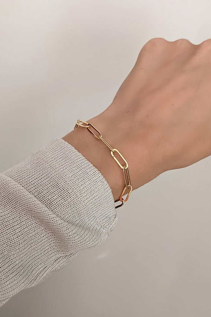 Gold bracelet on a wrist with a neutral background