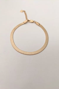 A gold herringbone bracelet with a sleek design, displayed against a neutral background.