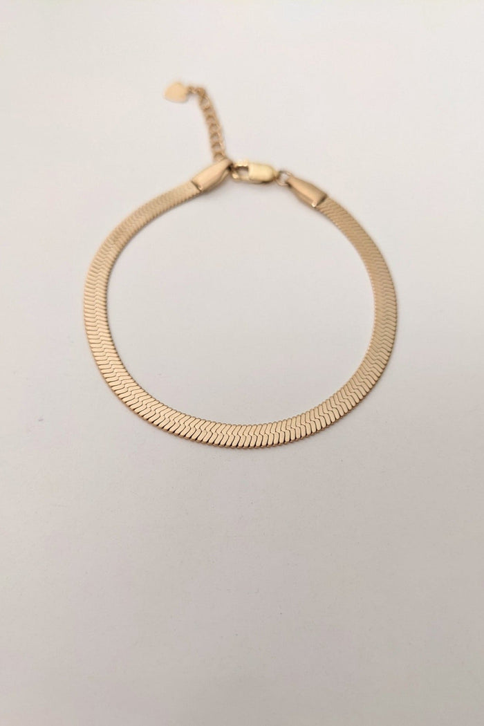 A gold herringbone bracelet with a sleek design, displayed against a neutral background.