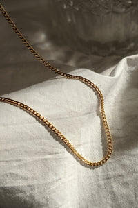 A gold-colored chain necklace laid out on a white fabric surface.