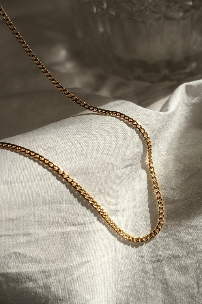 A gold-colored chain necklace laid out on a white fabric surface.